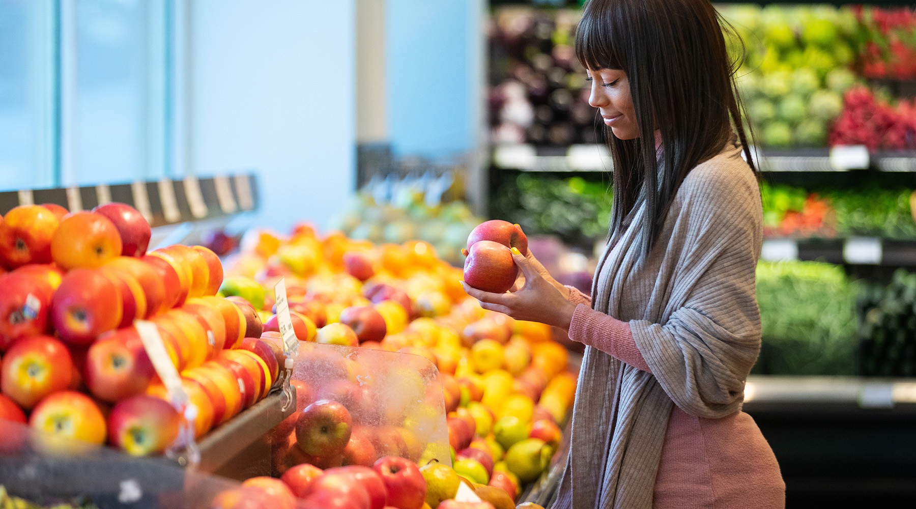 a woman at a fruit stand holding an apple a woman at a fruit stand holding an apple